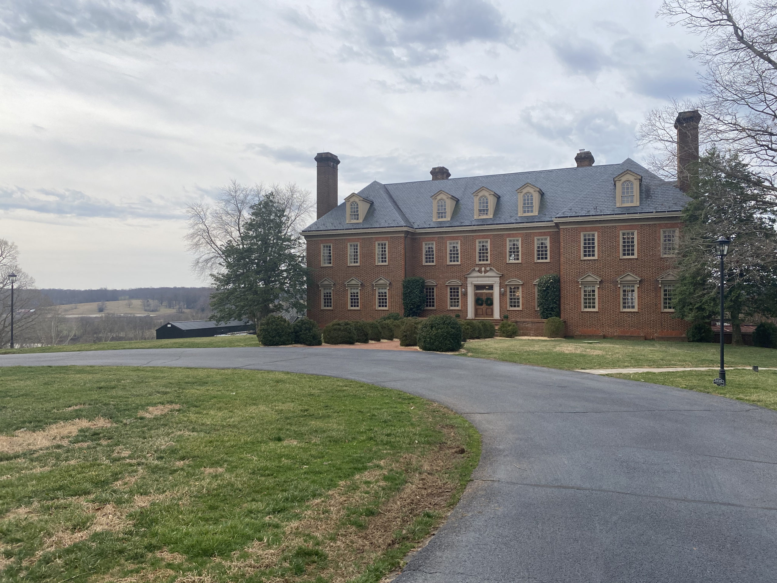 Brick estate surrounded by rolling hills and a circle drive.
