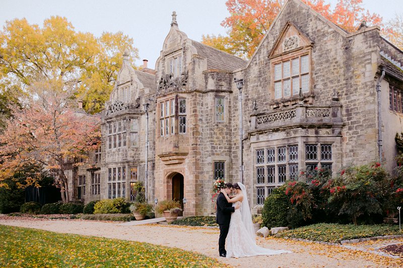 Stone manor house with a bridal couple embracing in the driveway