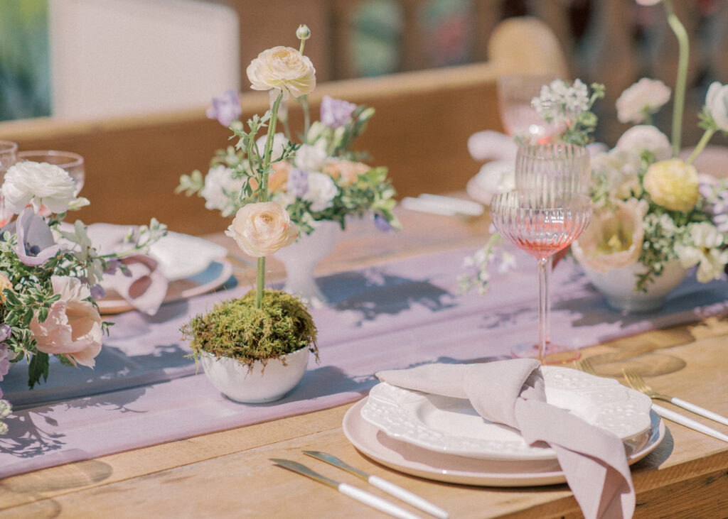 Oak table with pink glasses, floral centerpieces, and purple table runner.